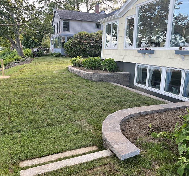 A well-manicured backyard with a curved retaining wall, fresh mulch, and a landscaping extension on a residential home.